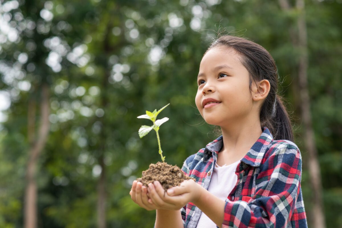 Asian girl standing at open space, close the eyes and hold the tree planted with smile, happy, love, care, share to reduce global warming for improve society, community and environment in the future